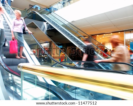 People in motion in escalators at the mall, with a golden banister at the foreground. Royalty-Free Stock Photo #11477512