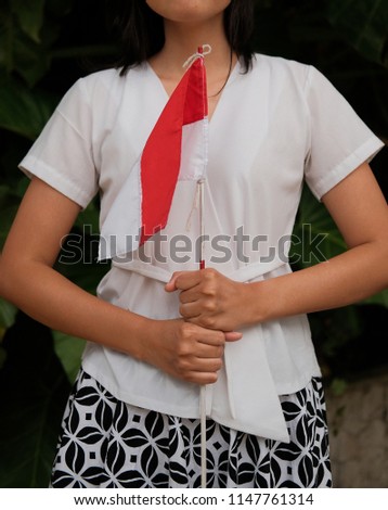 Indonesian woman grab red and white flag. Wearing white cloth and batik shirt. on floral background