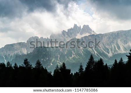 Italian Dolomites landscape. Light after rain in Dolomites. Rocky peaks in the background surrounded by rain clouds. Layers of forest and mountains ridge. Rocky Mountains Dolomiti. Storm rain 