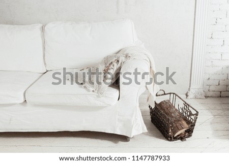 White sofa in a white room. Firewood in the basket