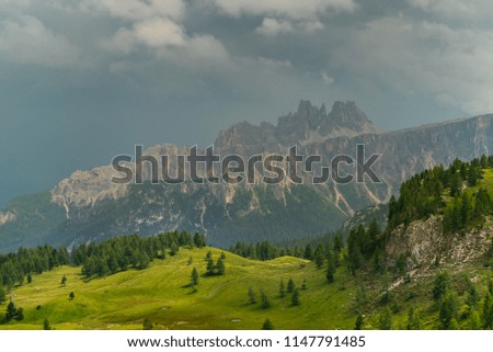Italian Dolomites Landscape. Light after rain in Dolomites. Rocky peaks in the background surrounded by rain clouds. Mountain valley with layers of forest and mountains. Beautiful light in Alps. Italy