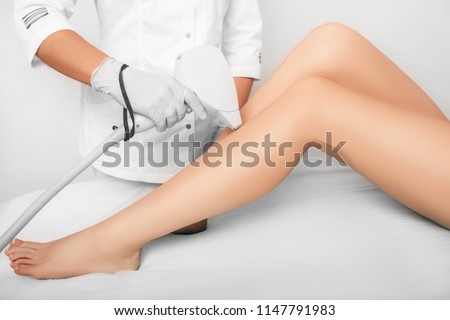 beautician removes hair on beautiful female legs using a laser. hair removal on the legs, laser procedure at clinic Royalty-Free Stock Photo #1147791983