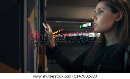 Stylish businesswoman enters the data on terminal at parking and makes payment. Female is touching an electronic screen on terminal