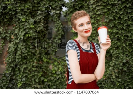 A woman with a short haircut on the street with a drink.                               
