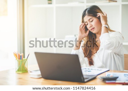 Asian woman with headache while working on laptop in her office
