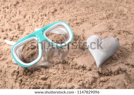Beach background image of a snorkel set and a heart shaped stone on a sandy beach  