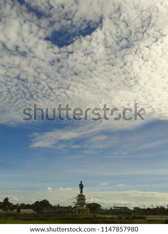 White cloud in blue sky high above walking buddha image 
