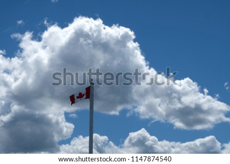 A Canadian Flag Is Blowing In The Wind With Clouds In the Background.