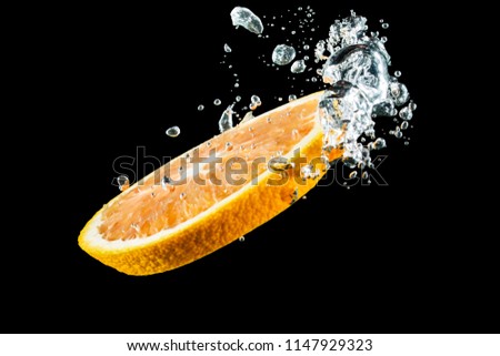 A slice of orange falls into the water with air bubbles on a black background
