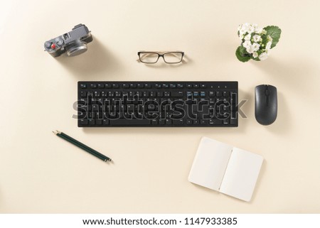Top view of desk with camera, flowers, keyboard, mouse, glasses, booklet and pencil, on a clean background