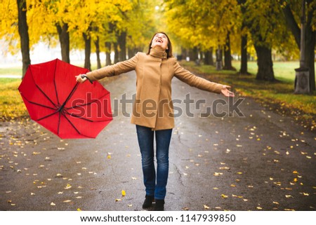Happy woman with red umbrella walking at the rain in beautiful autumn park. Concept picture