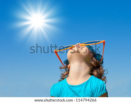 Happy little girl with big sunglasses looking at the sky with sun in summer Royalty-Free Stock Photo #114794266