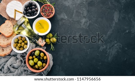 A set of green olives and black olives, bread, cheese and spices. On a black stone table. Free space for text.