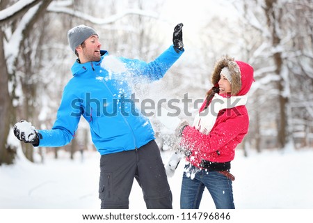 Carefree happy young couple having fun together in snow in winter woodland throwing snowballs at each other during a mock fight