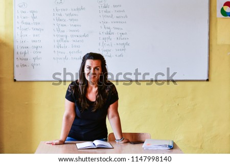 Smiling  happy  teacher standing in front of black board   while holding class register. 