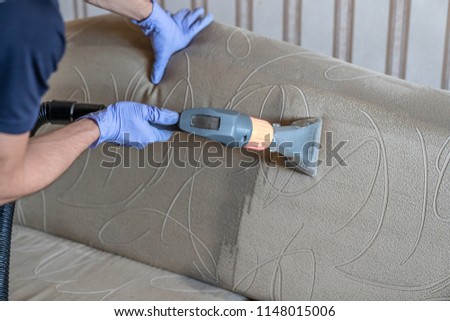 Closeup of upholstered Sofa chemical cleaning with professional extraction method. Man is holding nozzle. Royalty-Free Stock Photo #1148015006