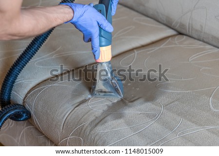 Closeup of upholstered Sofa chemical cleaning with professional extraction method. Man is holding nozzle. Royalty-Free Stock Photo #1148015009
