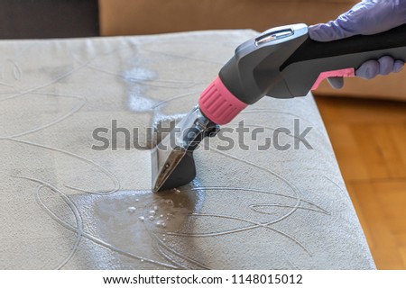 Closeup of upholstered Sofa chemical cleaning with professional extraction method. Man is holding nozzle. Royalty-Free Stock Photo #1148015012