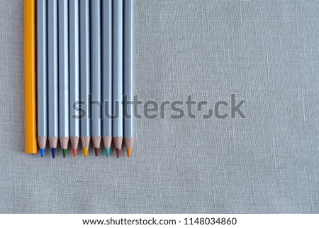 Colored pencils with one orange pencil on neutral background