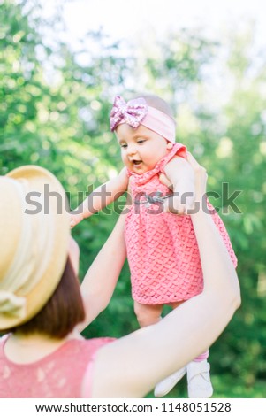 Beautiful Mother with the straw hat And her little daughter outdoors family look in in a pink dress . family look. Young mother throws up baby in the sky, on sunny day.