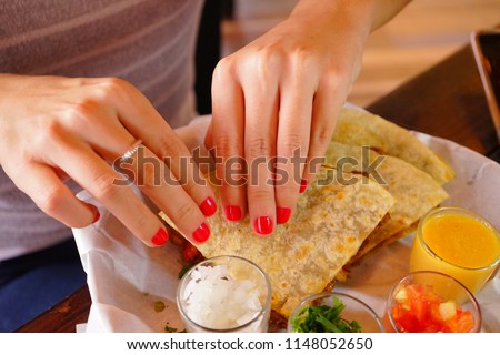 Hands of a woman eating a quesadilla of pork and melted cheese in some arina tortillas.