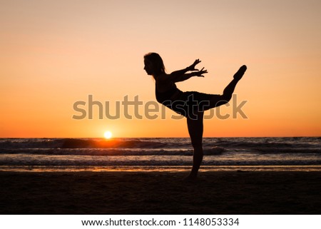 Silhouette of a girl practicing yoga on the beach at sunset
