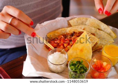 Hands of a woman eating a Quesadilla of pork and melted cheese in a tortillas.