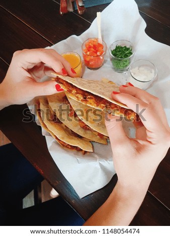 Hands of a woman eating a Quesadilla of pork and melted cheese in tortillas.