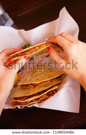 Hands of a woman eating a Quesadilla of pork and melted cheese in tortillas.