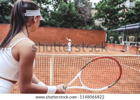 Child on serve!Cropped side view focused on beautiful tennis player with sporty child on blurred background.Young woman preparing to hit the serve from girl child on tennis court. Activities outdoors.
