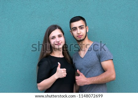 Waist-up portrait of cheerful loving couple dressed in trendy shirts. Sweet lovers showing thumbs up and posing for picture. Love concept. Isolated on mint background