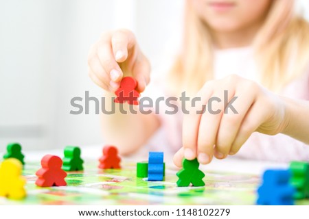 Board game and kids leisure concept - little blonde girl hold red people figure in hand. yellow, blue, green wood chips in children play Royalty-Free Stock Photo #1148102279