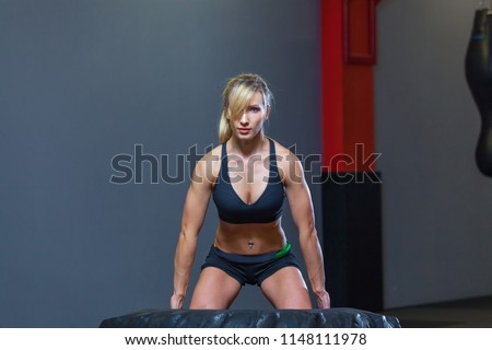 Fit female athlete working out with a huge tire, turning and carry in the gym. Crossfit woman exercising with big tire