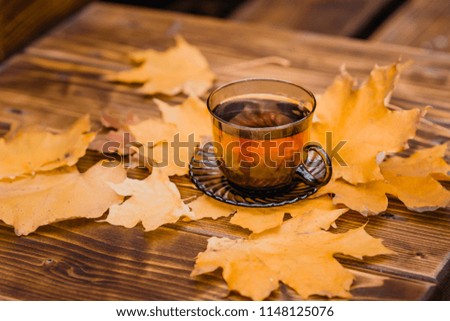 a cup of tea and yellow leaves on a wooden table