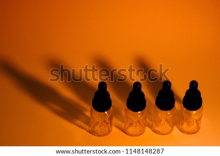 Four glass eye dropper bottles with dark black shadows on golden orange background. A little noise added for effect.
