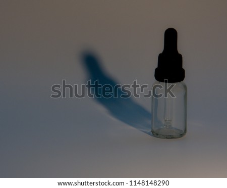 Closeup of single eye dropper bottle with blueish shadow on gray background.  A little noise added for effect.