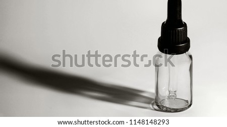 Closeup of single eye dropper bottle with strong dark shadow on white background. 
