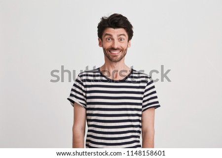 Portrait of happy attractive young man with bristle wears striped t shirt feels excited and smiling isolated over white background Looks directly in camera