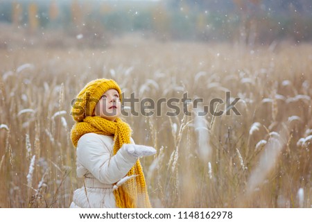 A little girl in a yellow hat is fascinated to look at the first falling snowflakes and tries to catch them with her hand Royalty-Free Stock Photo #1148162978