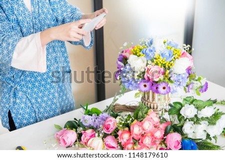 young women business owner florist taking photo Artificial flowers vest with smart phone in her own shop for promote website, craft and hand made concept.