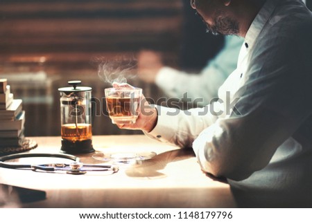 The picture of Asian or Muslim doctor take a break with hot tea cup with vapor steam.Stethoscope and a stack of books put beside.Sunlight shining upon.Light and shade of evening.Quiet,peace and relax.