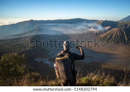 Tourist is standing on the viewpoint of the hill for take a look the beautiful scenery of fog, volcano and take picture by cell phone in the morning at Bromo Tengger Semeru National Park, Indonesia.