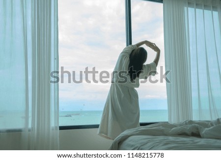 Behide asian woman in bathrobe suit open curtain to see view outside in morning, Travel and Holiday concept