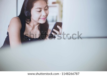 Beautiful girl is relaxing at home. She is listening to music, wearing headphones and holding a phone.Selective focus.