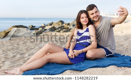 Young loving couple resting and taking selfie on the beach 
