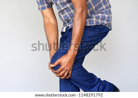 Pain In Knee. Close-up African Male Leg With Painful Kneeson on gray background. Man Feeling Joint Pain, Having Health Issues And Touching Leg With Hands. Body And Health Care Concept.