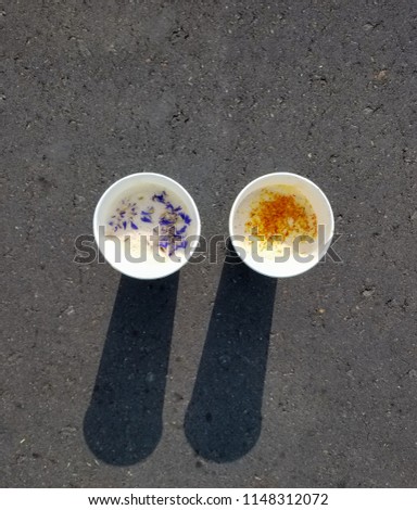 Two cups of coffee with cornflowers and saffron standing on asphalt with shadows of its