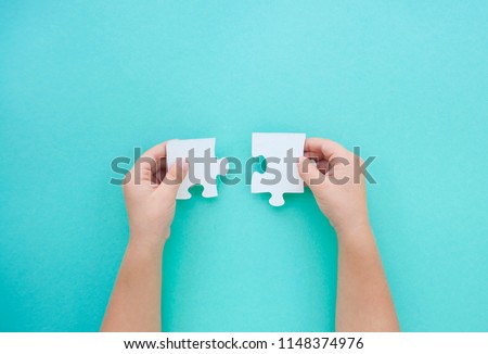 Child's hands holding two puzzle pieces on blue background as a symbol of autism awareness.