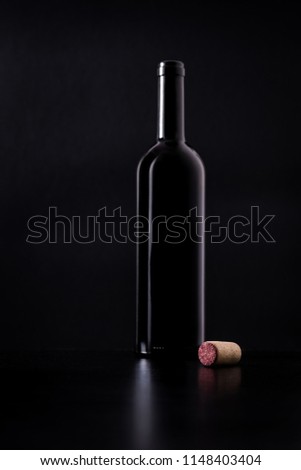 Red wine cork with silhouette of red wine bottle behind isolated on black dark background with soft reflections and beautiful shadows. Shallow depth of field