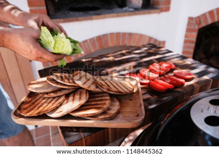 Close-up of male chef hands preparing burgers of buns cooked on grill, squid cutlets, melded cheese, lettuce and tomato. Ingredients for squid burgers.